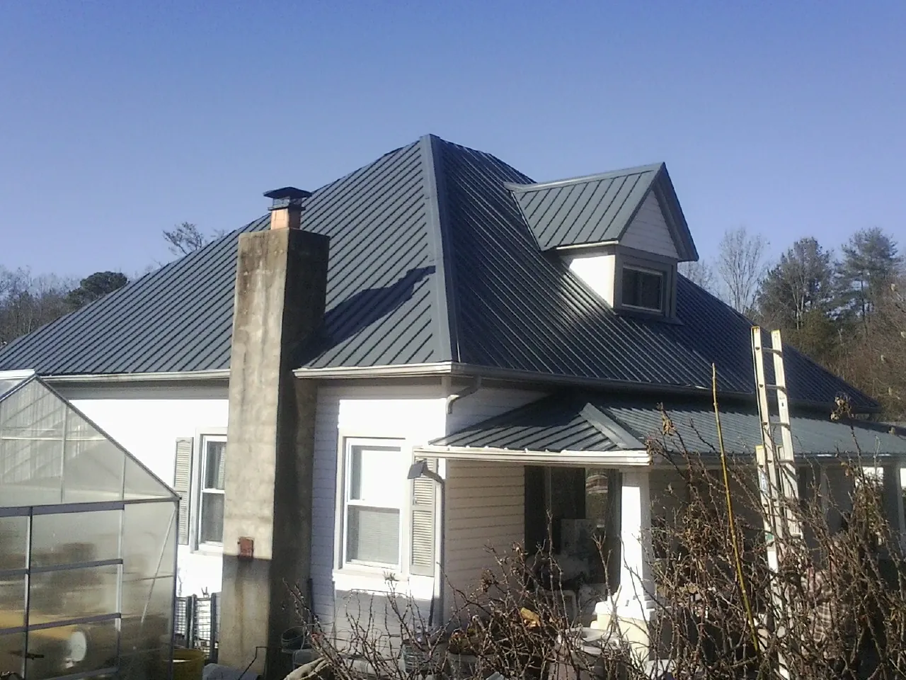 Dark blue standing seam metal roof on a white farmhouse with dormer — Slate & Tile Roof Repair by Roofing Brothers in East Falmouth