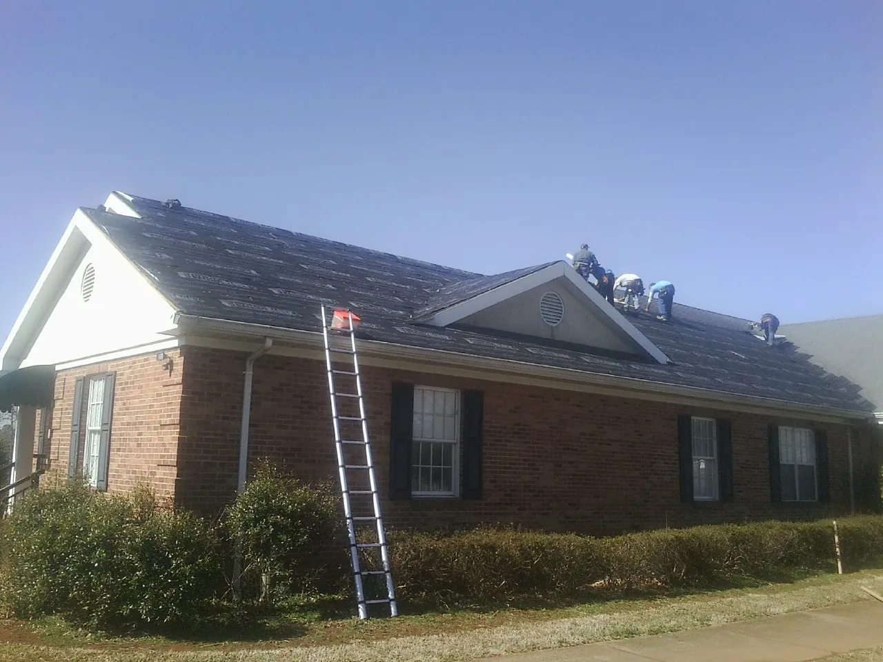 Crew tearing shingles off a brick ranch roof with a ladder set — Metal Roof Repair work by our crew in East Falmouth