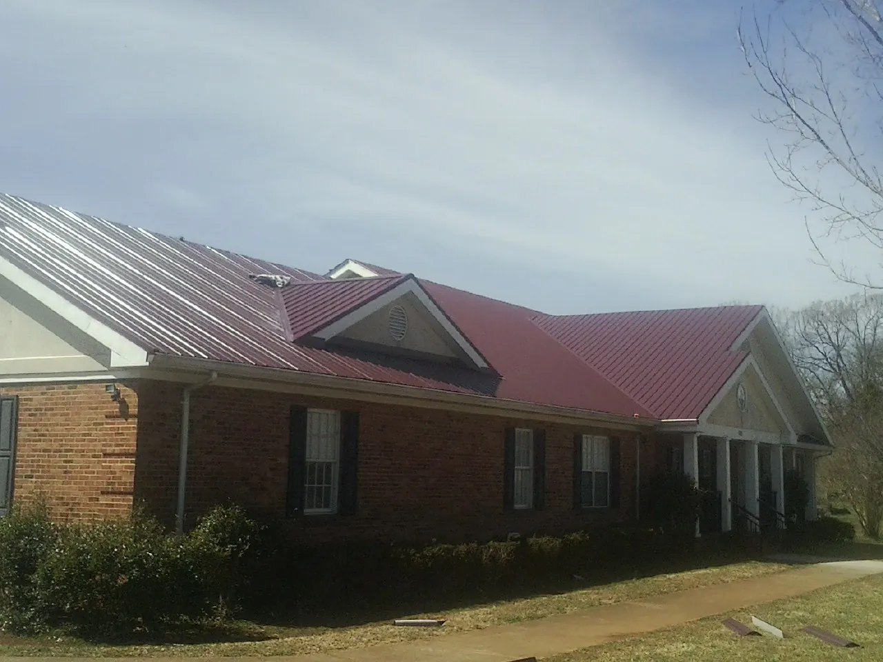 Red metal roof with gabled entries on a long brick building, from a Hail Damage Roof Repair job in East Falmouth
