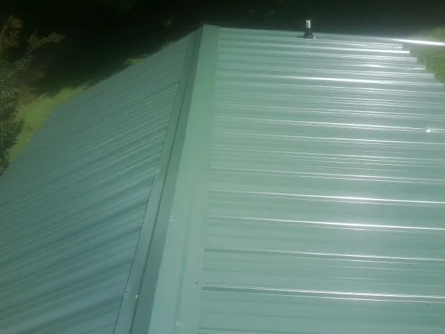 New green metal panels meeting at the ridge of a roof — Flat Roof Repair work by our crew in East Falmouth