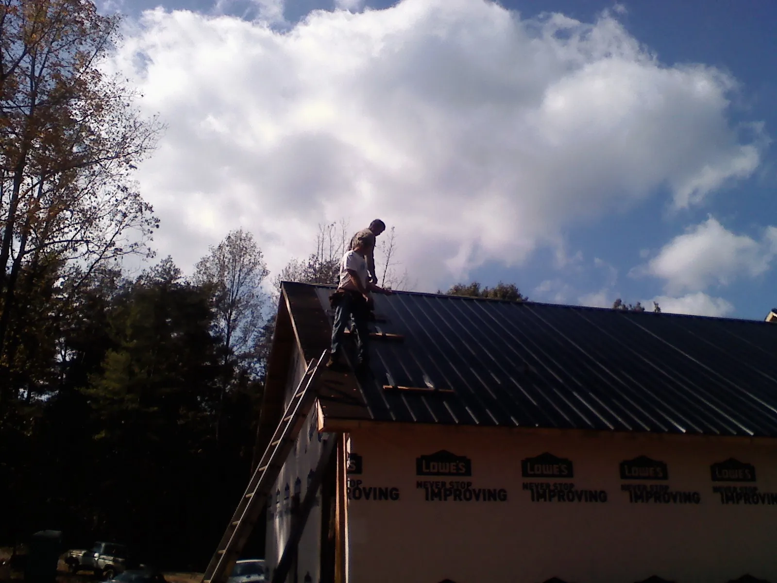 Roofer fastening dark metal panels high against a cloudy sky, from a Roof Inspection job in East Falmouth