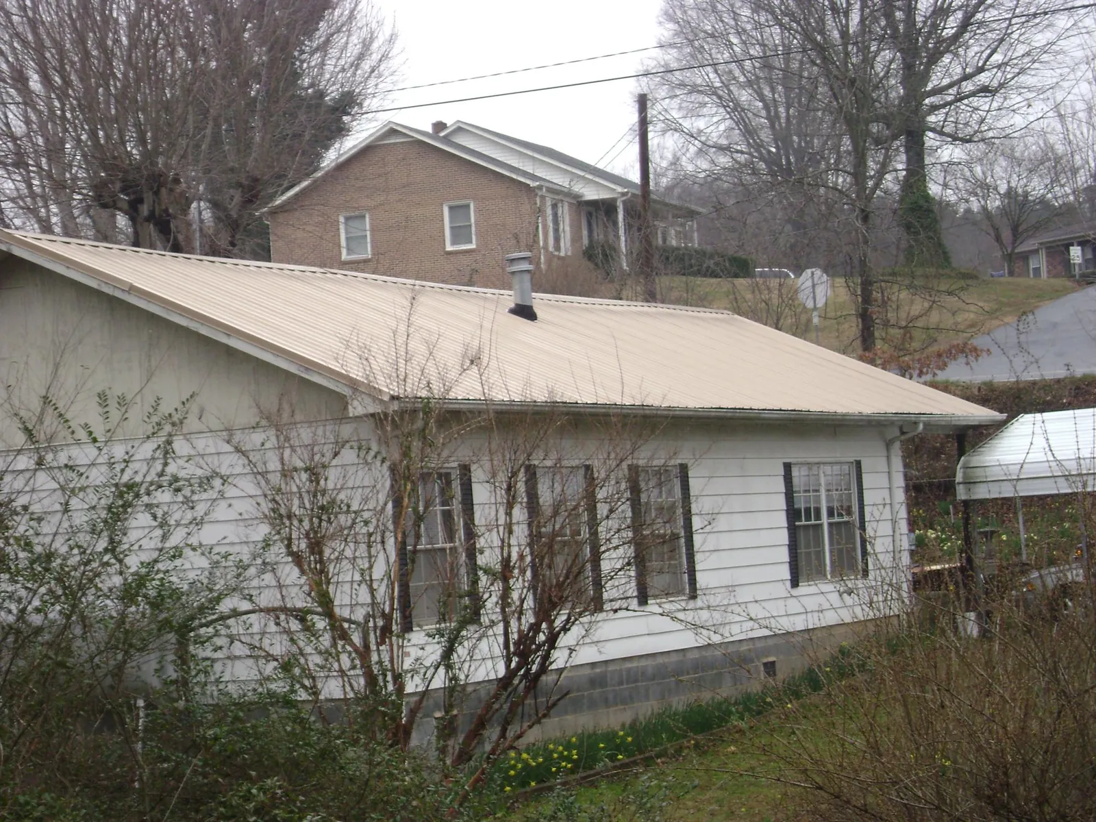 Tan metal roof on a white sided house set into a hillside — Commercial Roofing by Roofing Brothers in East Falmouth